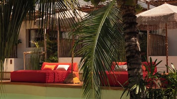 A poolside area with a red lounge chair, a palm tree, and a red sofa with cushions.