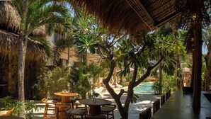 An outdoor lounge area with tables and chairs, surrounded by palm trees and a pool. - Divino Gili Air (Gili Air)