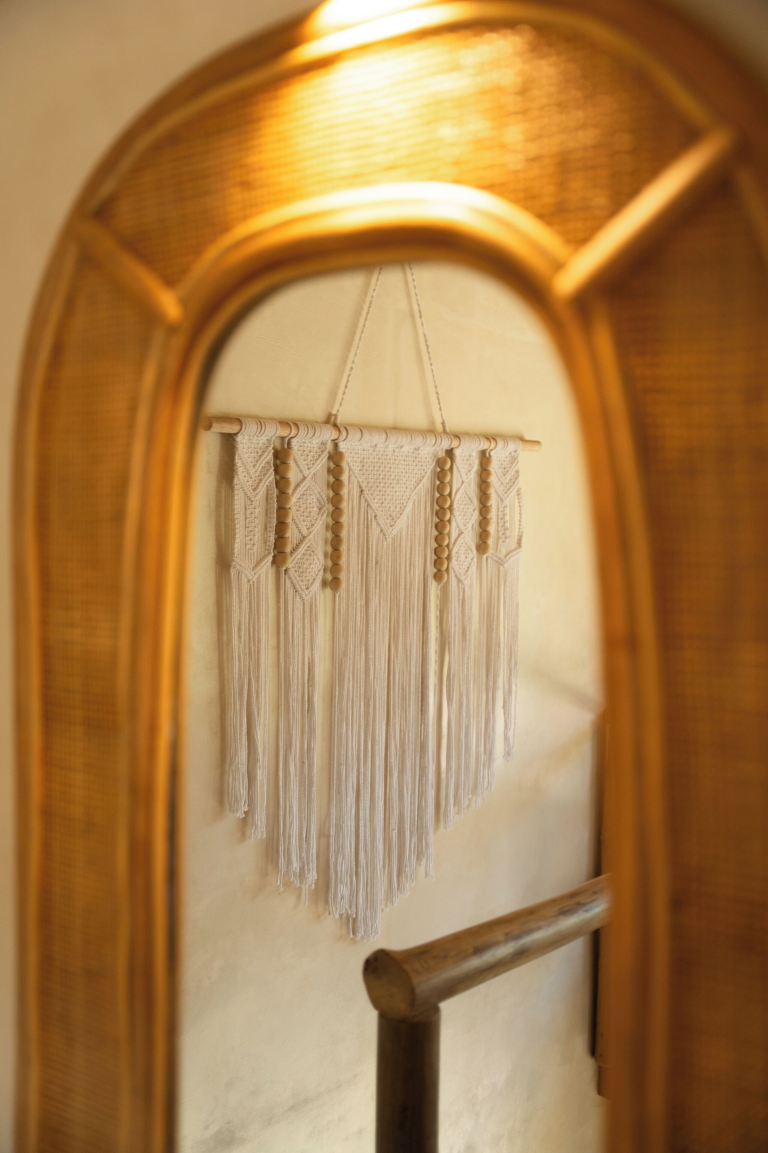 Un tapiz de macramé con borlones y patrones geométricos, colgado de un marco de madera.