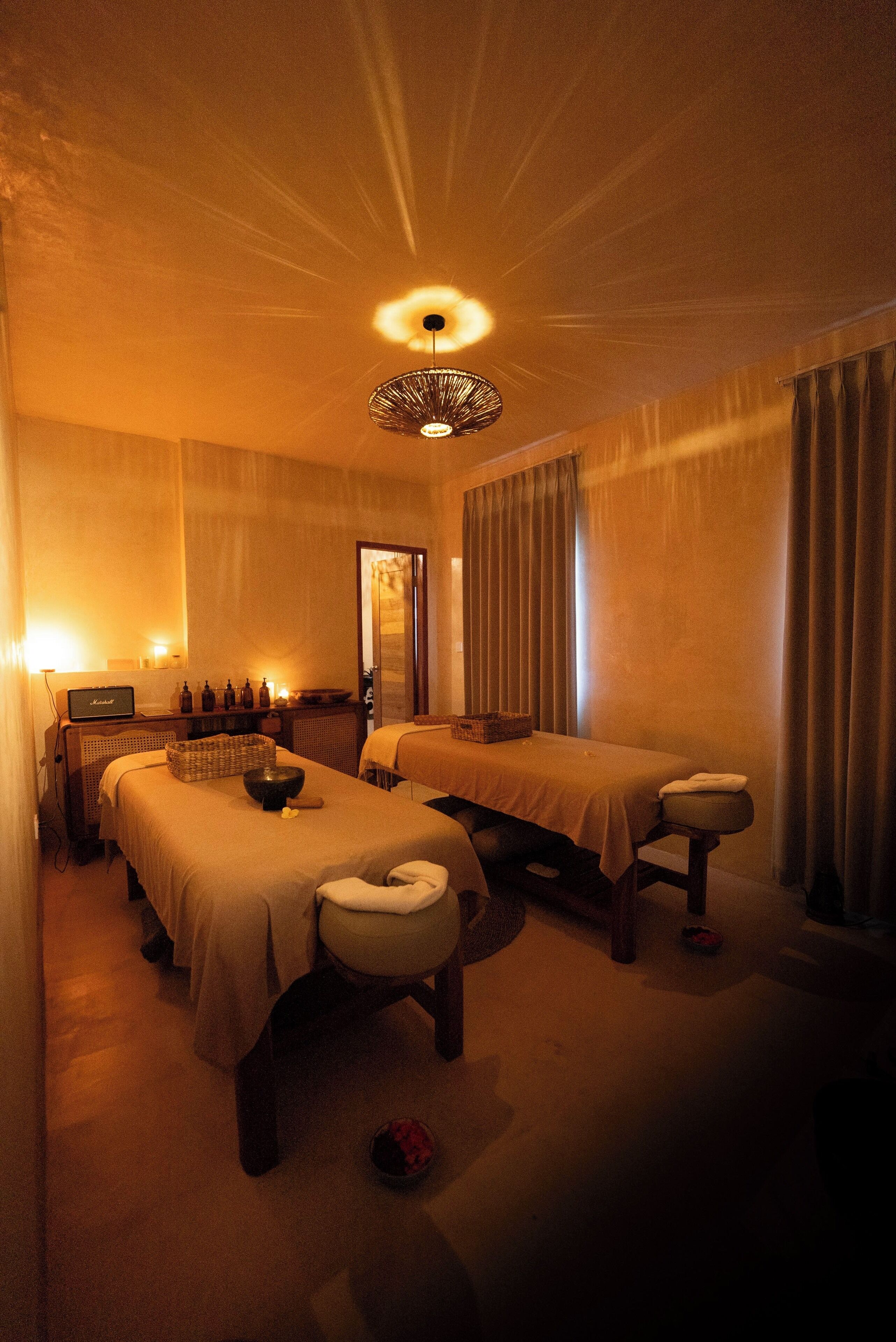 Ein Spa-Raum mit zwei Massagetischen, einer Deckenleuchte und einem kleinen Empfangstresen.