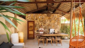 A room with a stone wall, a wooden table with chairs, a hanging chair, and a sofa with cushions. - Divino Gili Air (Gili Air)