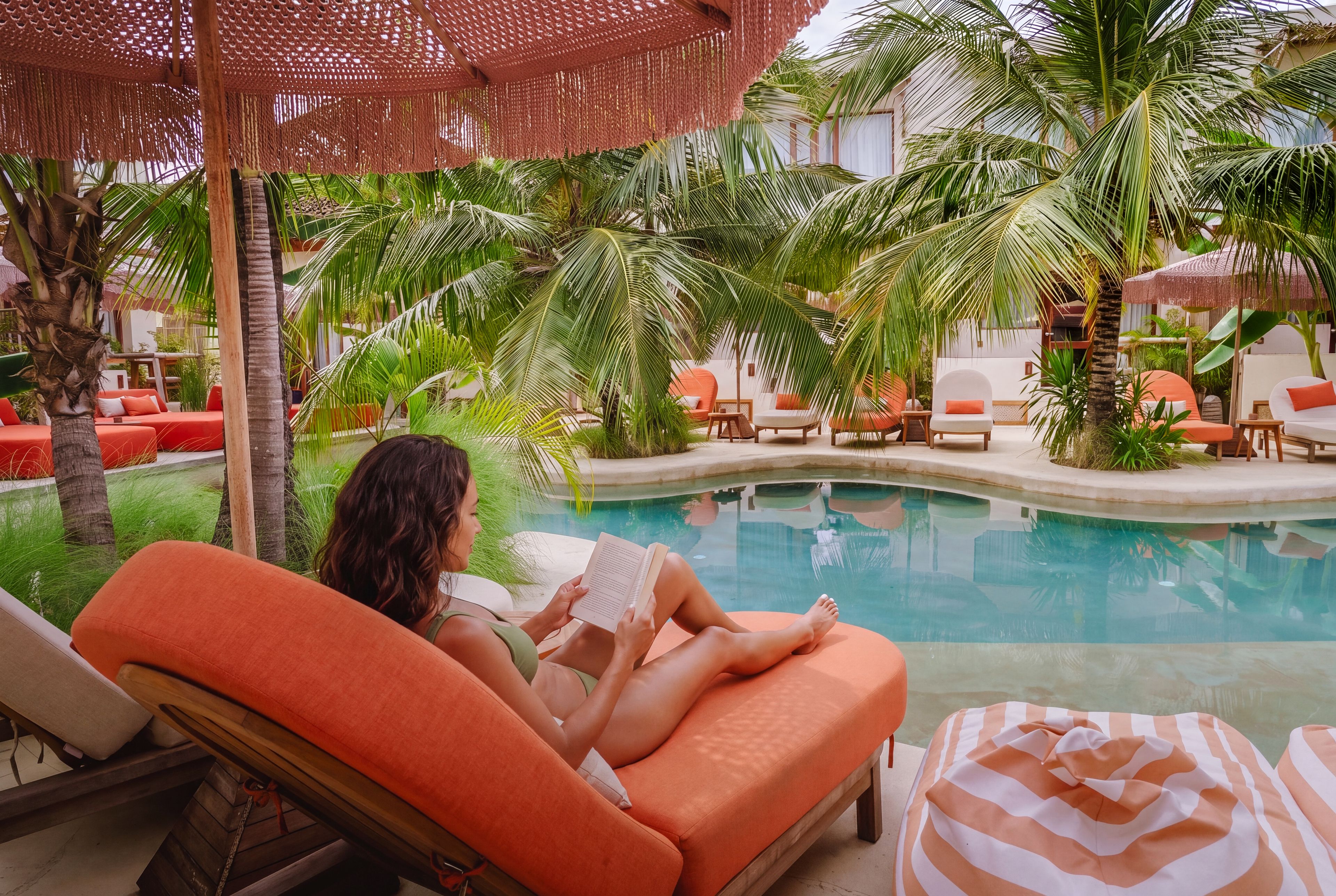 A poolside lounge area with orange seating, palm trees, and a clear pool.
