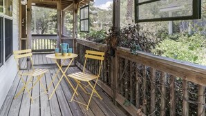 A wooden deck with a table and chairs, a railing, and a view of greenery. - The Jasmine Loft (Tybee Island)