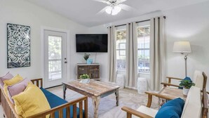 A living room with a wooden sofa, a coffee table, a TV, and a window with curtains. - The Jasmine Loft (Tybee Island)