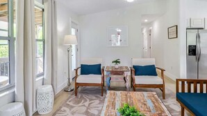 A modern living room with a ceiling fan, a coffee table, two sofas with cushions, a side table, and a refrigerator. - The Jasmine Loft (Tybee Island)