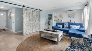 Una sala de estar con un sofá azul, una mesa de centro blanca y una puerta blanca rústica.