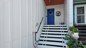 Fachada blanca con puerta azul, escalones blancos y plantas en macetas.