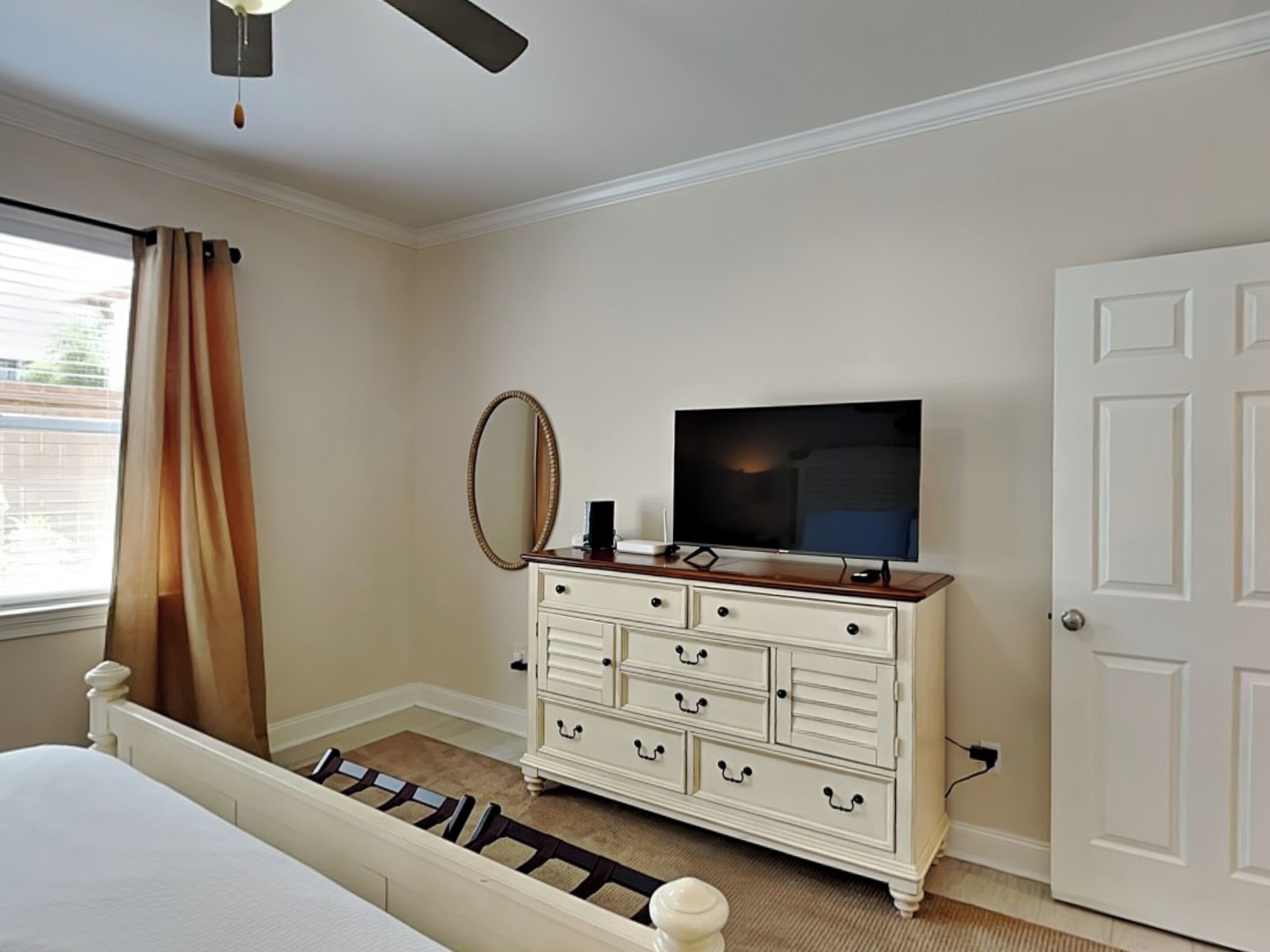 Une chambre à coucher avec un lit, une commode, un téléviseur et une porte.