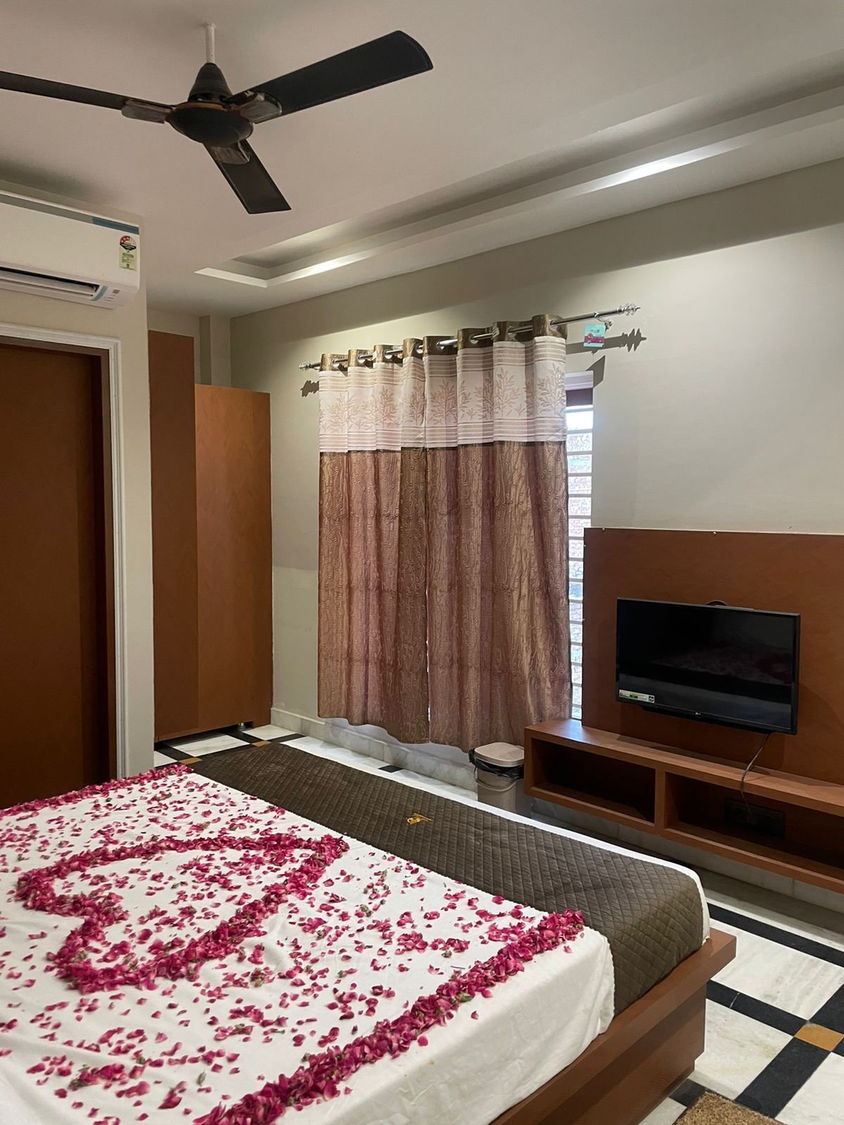 Une chambre d’hôtel avec un lit, un ventilateur de plafond, une télévision et une fenêtre avec des rideaux.