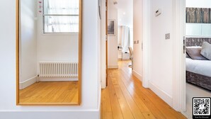 Un interno moderno con pavimento in legno, pareti bianche, un termosifone e un letto con testiera.