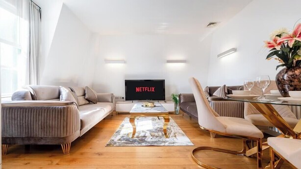 Un soggiorno moderno con un divano, un tavolo da pranzo con sedie e una TV a schermo piatto che mostra il logo di Netflix.