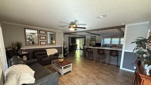 A spacious living room with a dark leather sofa, a coffee table, and a dining area with bar stools.