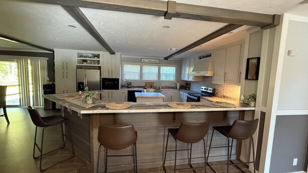 A modern kitchen with a large island, bar stools, and a dining area with a view of the outdoors.