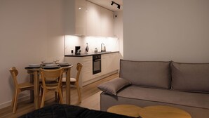 A modern kitchen with white cabinets, a dining table with chairs, and a grey sofa with a small wooden table in the living area. - Apartamenty Sun & Snow Nadmorska Florina (Leba)