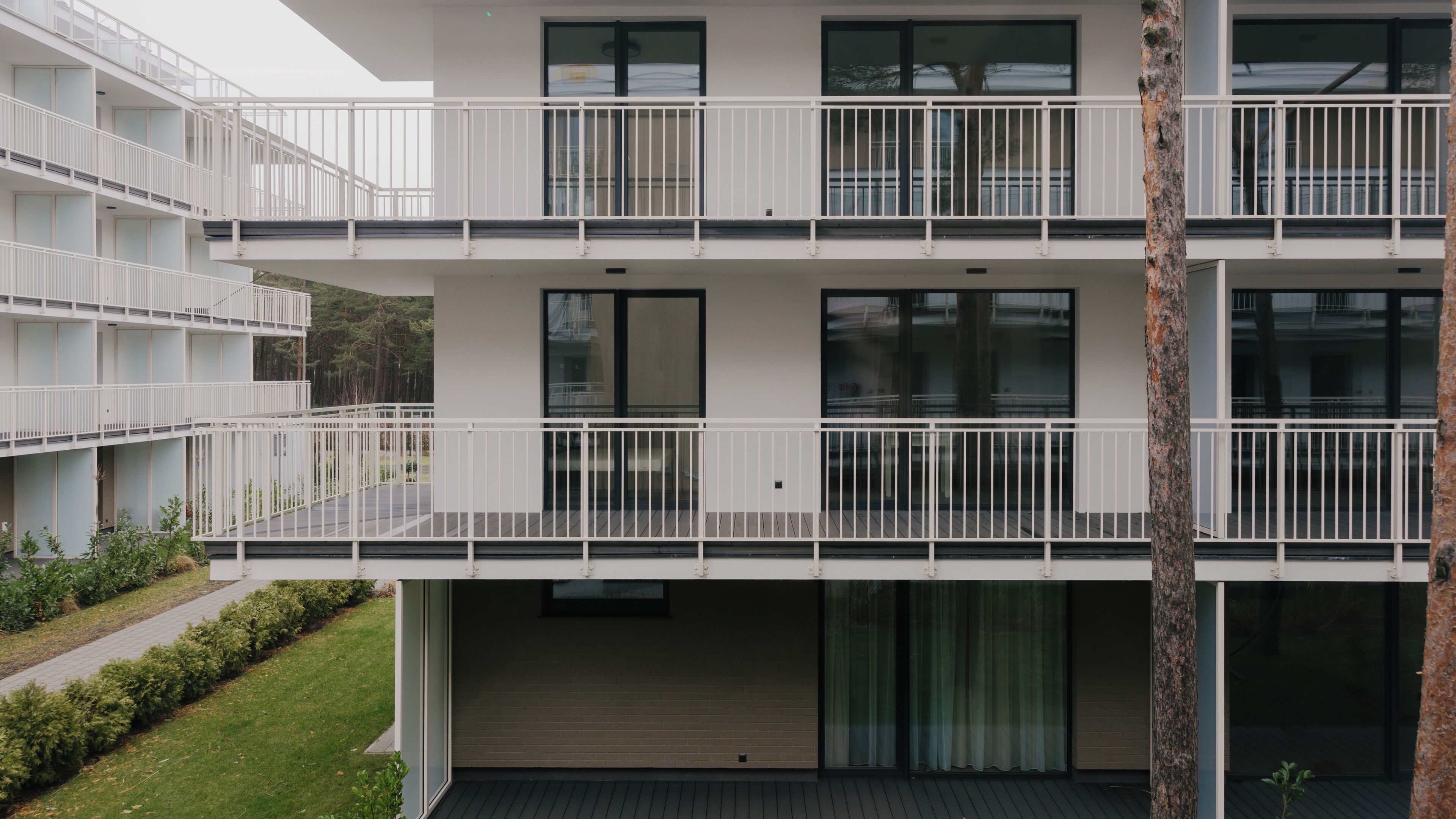 A modern multi-story building with balconies, large windows, and a flat roof.