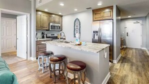 A modern kitchen with wooden cabinets, a central island with stools, stainless steel appliances, and a decorative wall piece.