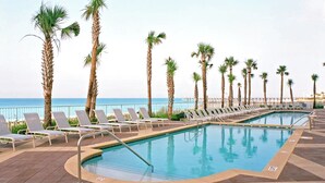 A poolside area with lounge chairs and palm trees, overlooking the sea.