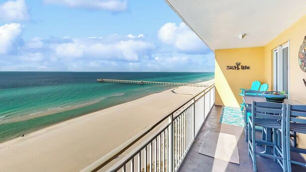 A balcony with a view of the beach and ocean, a table with chairs, and a sign that reads "Sail Life".