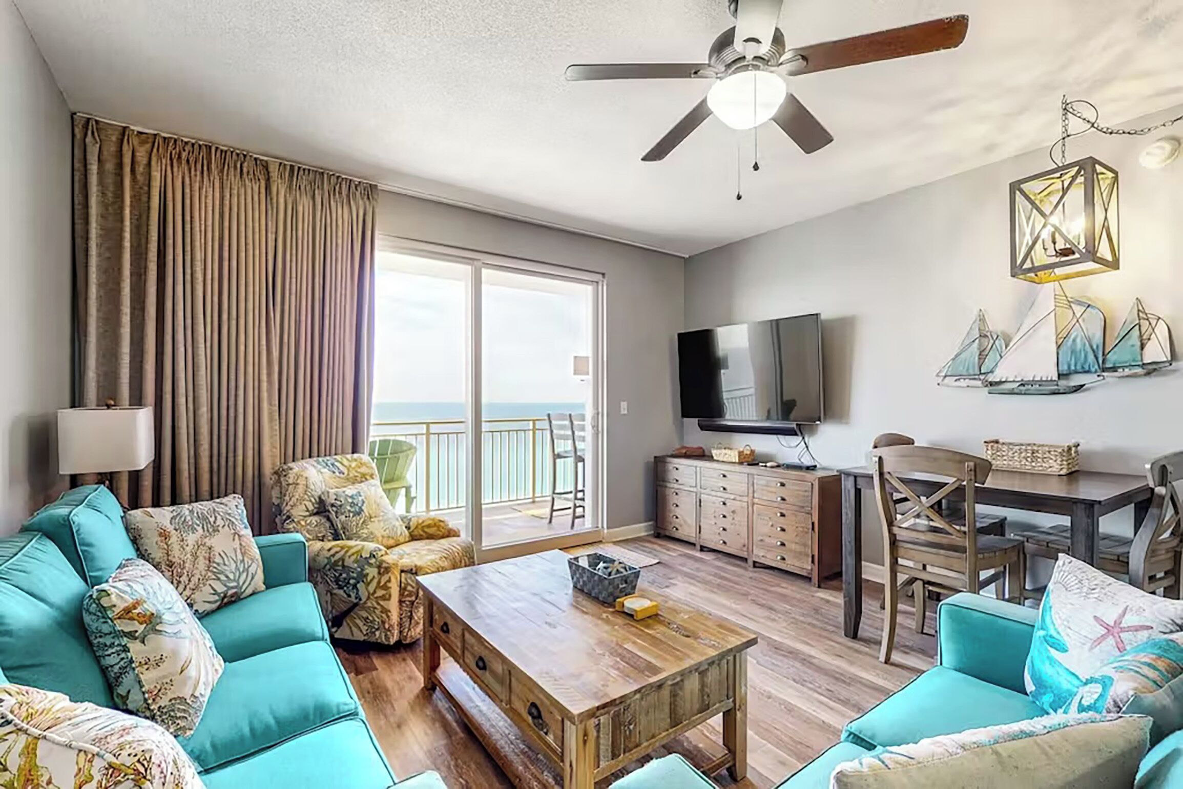 A spacious living room with a sofa, coffee table, and a TV. There is a balcony with a view of the ocean.