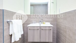 A bathroom with a white sink, two wooden cabinets, and a towel hanging on a rack. - Bloomfields Cozy STU Balcony Leonardo (Abu Dhabi)