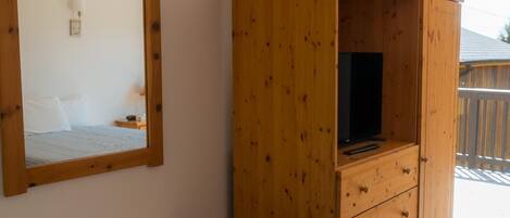 Ein Zimmer mit weißem Tisch und Stühlen, einem Holzschrank mit Fernseher und einem Spiegel an der Wand.