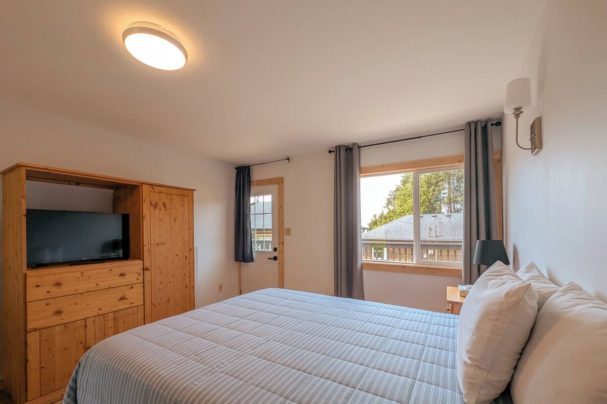 Une chambre à coucher comprenant un lit, une armoire en bois, un téléviseur, une fenêtre avec des rideaux et une lampe fixée au mur.