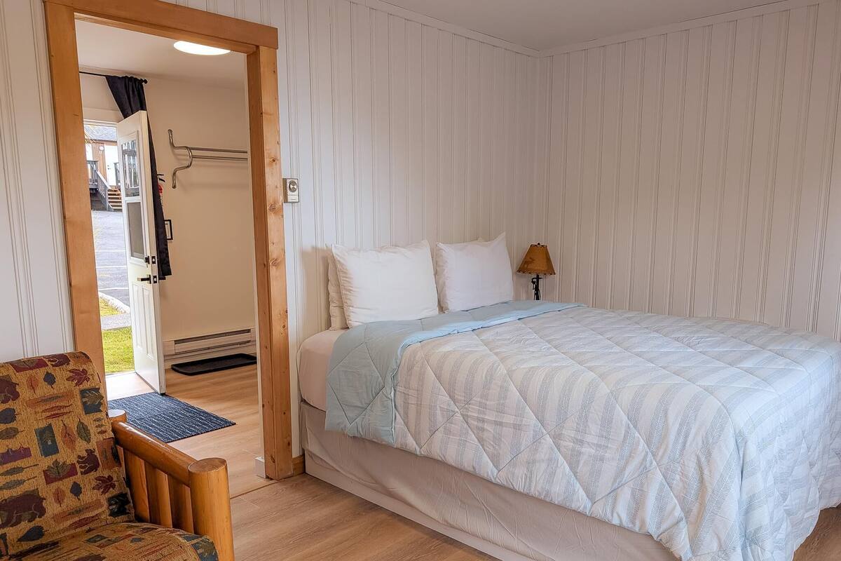 Une chambre à coucher comprenant un lit, une chaise, une lampe et une porte donnant sur un balcon.