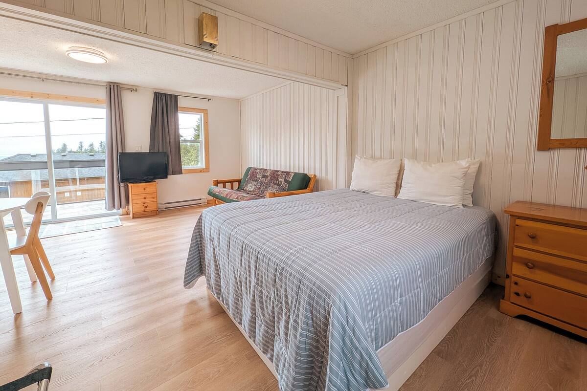 Une chambre à coucher avec un lit, une télévision, une chaise, une commode et une fenêtre avec des rideaux.
