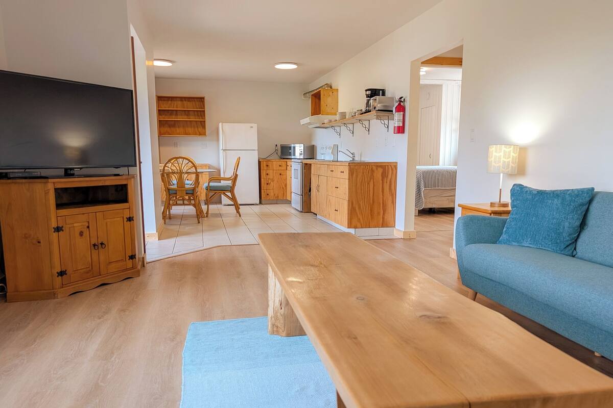 Un salon moderne avec une table basse en bois, un canapé bleu et un téléviseur posé sur un meuble en bois.