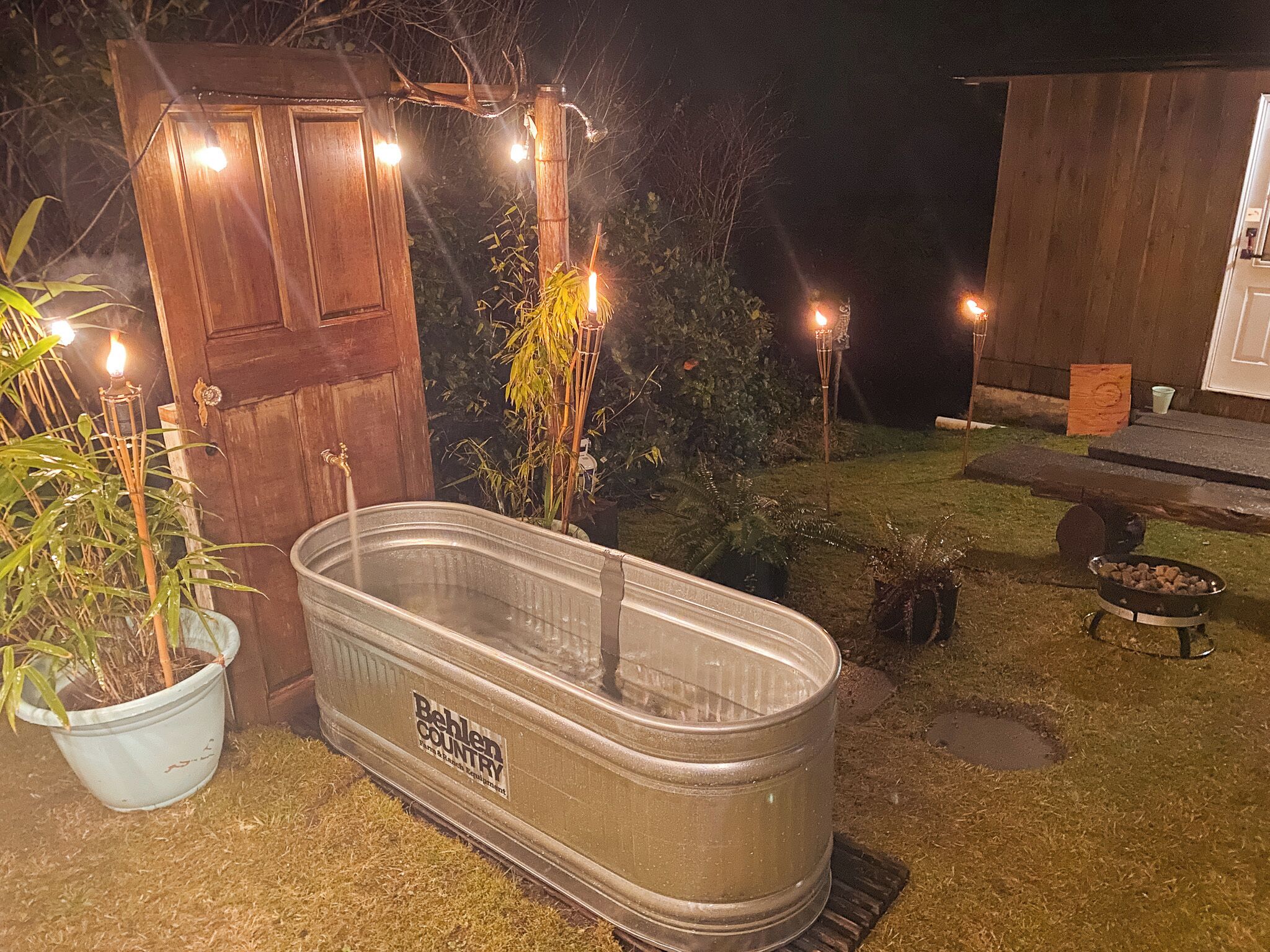 Un bain à remous extérieur, muni d’une étiquette, entouré de plantes en pot et d’une structure en bois.