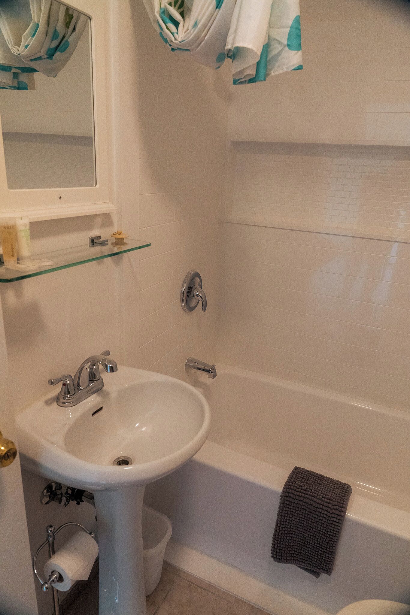 Un baño con un lavamanos blanco, un estante de vidrio, un espejo y una bañera.