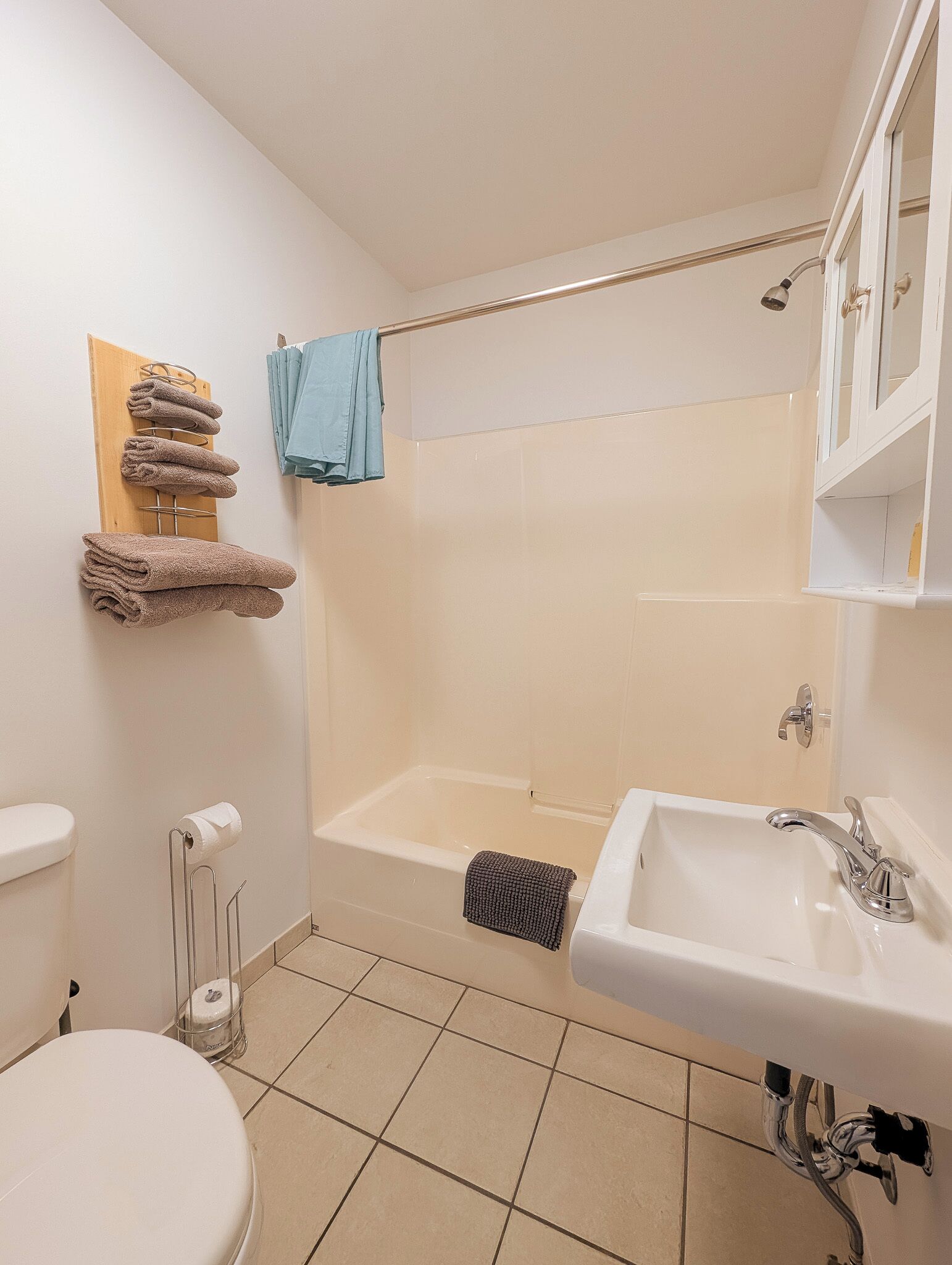 Une salle de bain avec une baignoire, un lavabo et des toilettes. Des serviettes sont suspendues sur un porte-serviettes et une serviette bleue est posée sur une barre à serviettes.