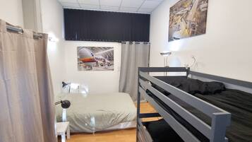 Een slaapkamer met een stapelbed, een bureau, een stoel, een lamp, een raam met gordijnen en een poster aan de muur.