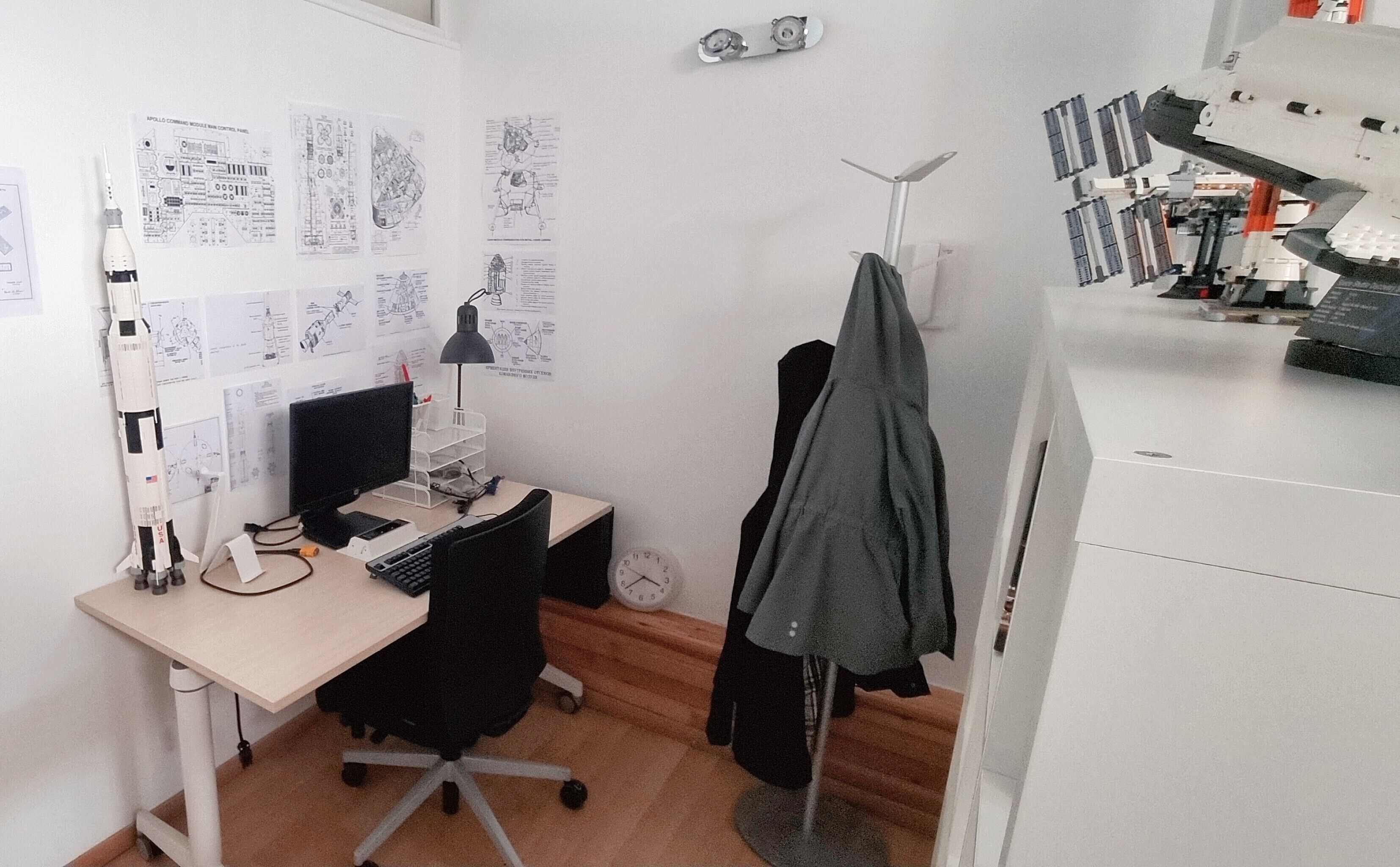 Een klein kantoor met een bureau, computer en diverse documenten en tekeningen aan de muur.