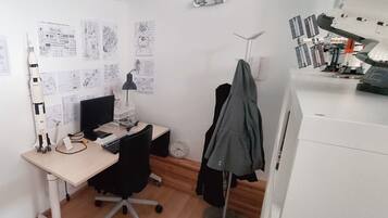 Een klein kantoor met een bureau, computer en diverse documenten en tekeningen aan de muur.