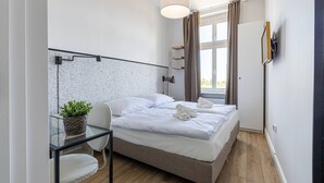 A modern hotel room with a bed, a desk, a chair, a potted plant, and a window with curtains. - Verde 5 Pok j Wifi Dolny Gda sk (Gdansk)