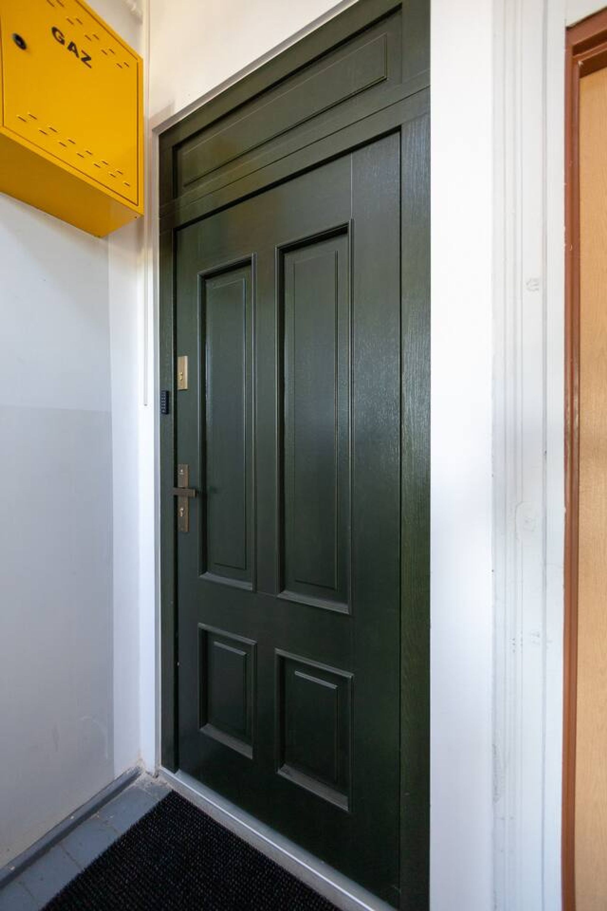 A dark green door with a brass handle and a yellow fire alarm box above it.