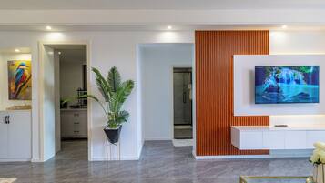 A modern living room with a flat-screen TV mounted on a white wall, a potted plant, and a wooden accent wall.