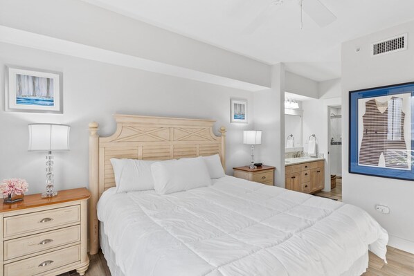 A bedroom with a large bed, a wooden headboard, bedside tables with lamps, and framed artwork on the walls.