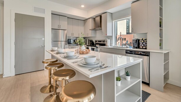 Una cocina moderna con armarios blancos, electrodomésticos de acero inoxidable y una isla central con taburetes.