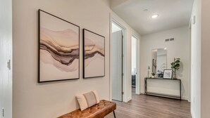 Ein modernes Interieur mit einer Holzbank, zwei abstrakten Gemälden und einem Konsolentisch mit Dekorationen.