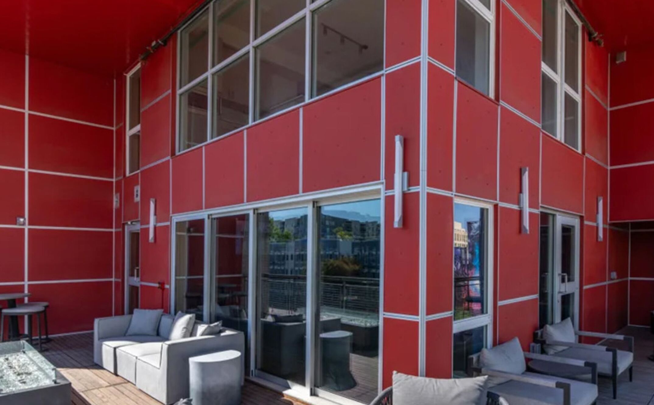 Una terraza en la azotea con fachada roja, puertas de cristal y mobiliario exterior.