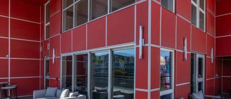 Una terraza en la azotea con fachada roja, puertas de cristal y mobiliario exterior.