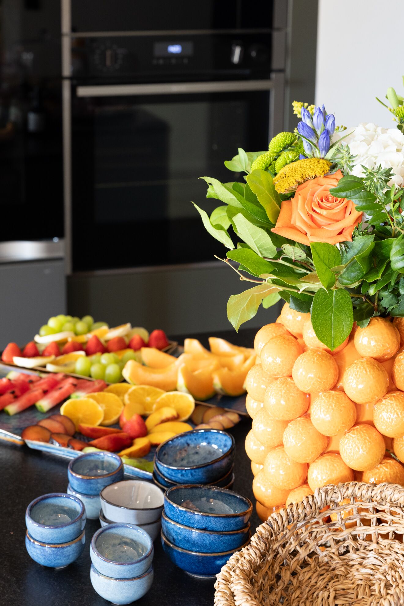 A kitchen counter with a fruit platter, a pineapple, and a vase with flowers.