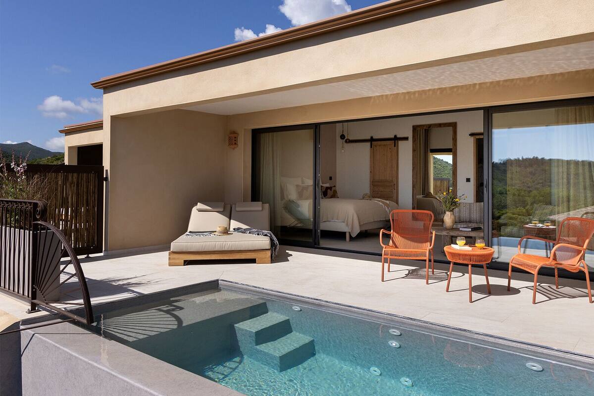 Un espace piscine extérieur moderne, doté d’une chambre fermée par des parois de verre et de chaises orange.