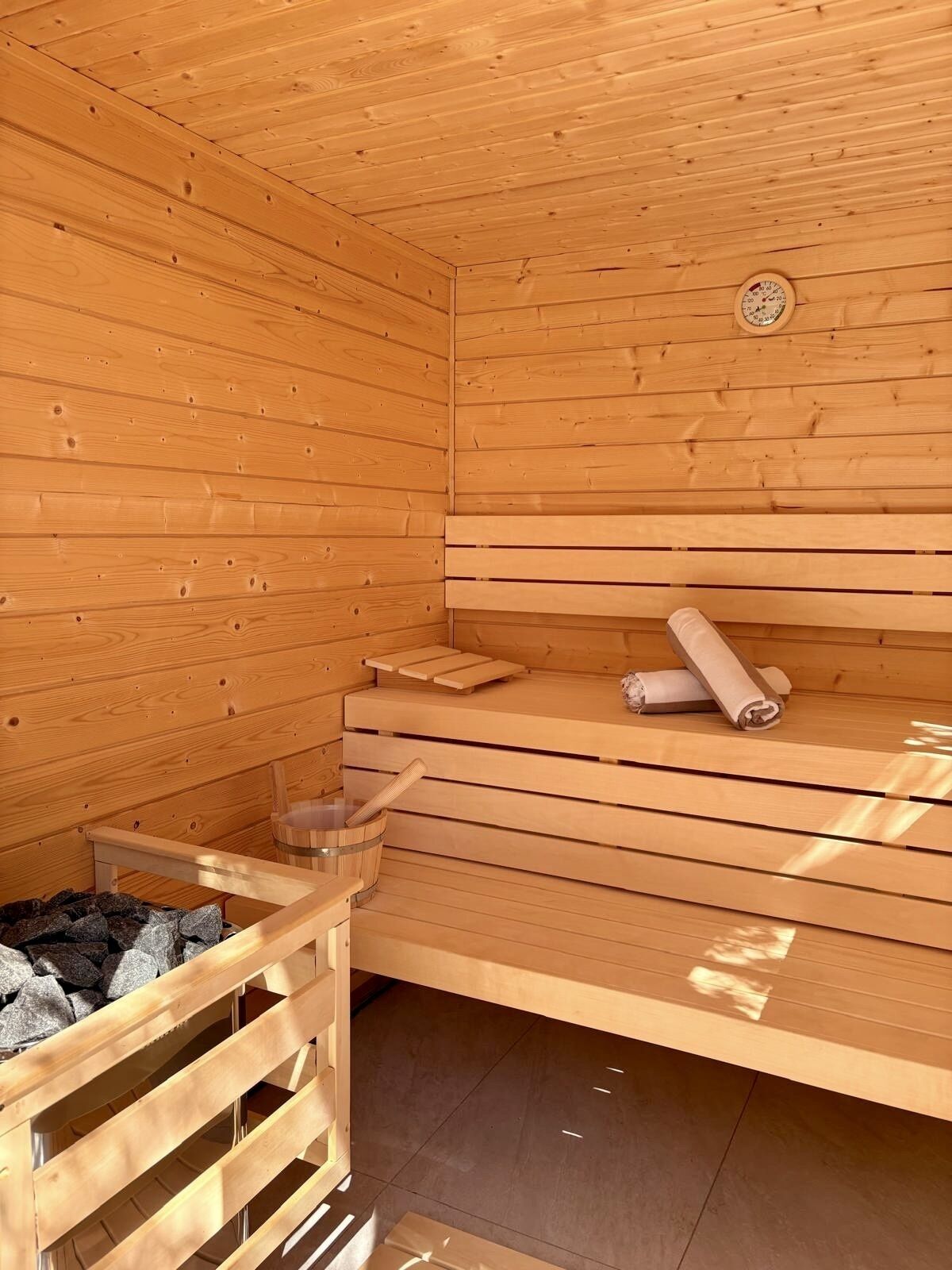 Una sauna de madera con bancos, un banco de madera, un termómetro de sauna y un balde.
