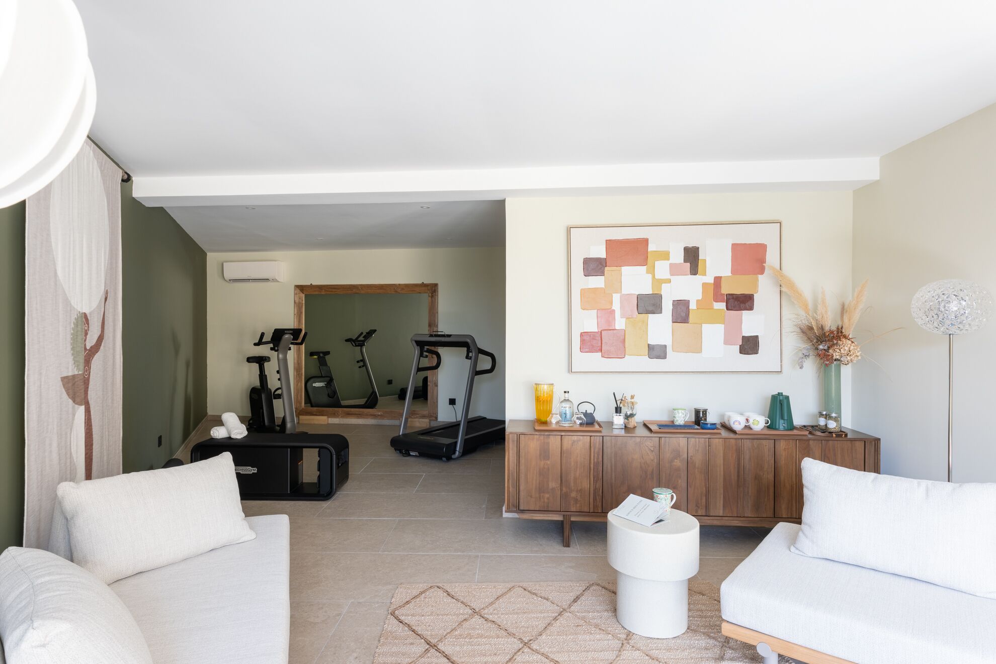 Una sala de estar con un sofá, una mesa de centro, un mueble con objetos y una cinta de correr al fondo.