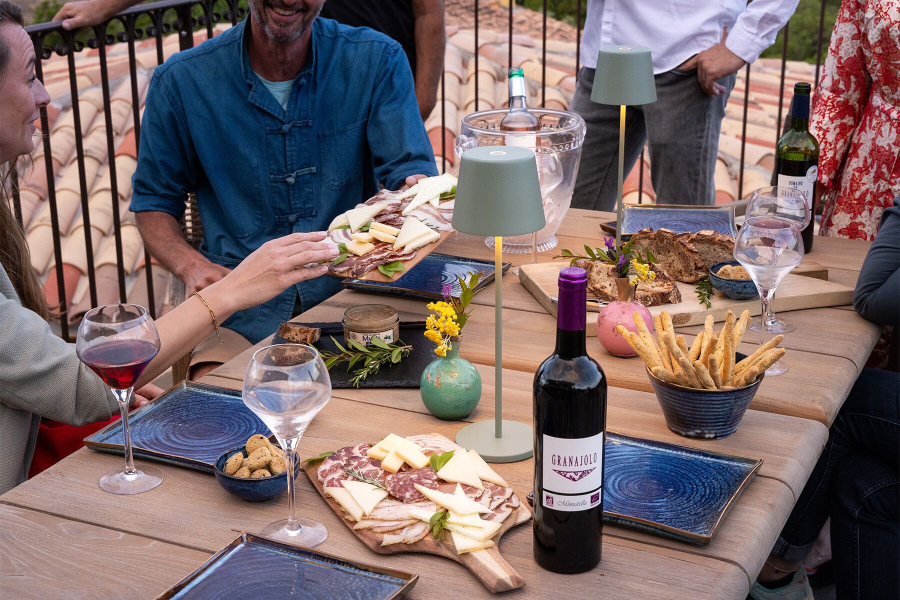 Una mesa de madera con diversos alimentos, como queso, pan y una botella de vino, lo que sugiere un ambiente de comedor informal.