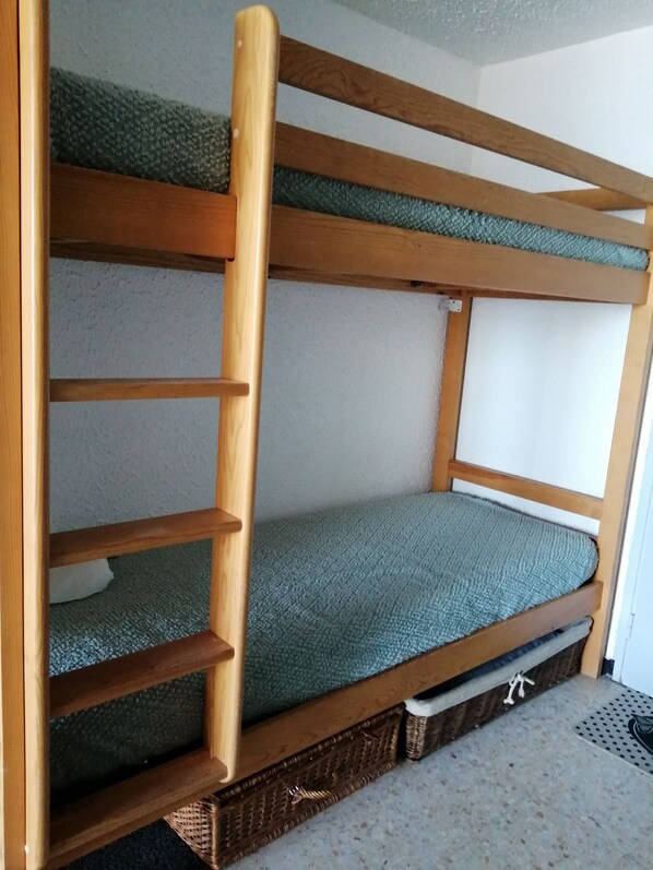 A bunk bed with a wooden ladder, a green mattress, and a woven basket at the foot.