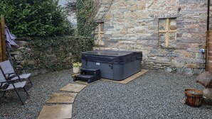 A stone building with a hot tub, a chair, and a small table. - Cader Cottage (Dolgellau)